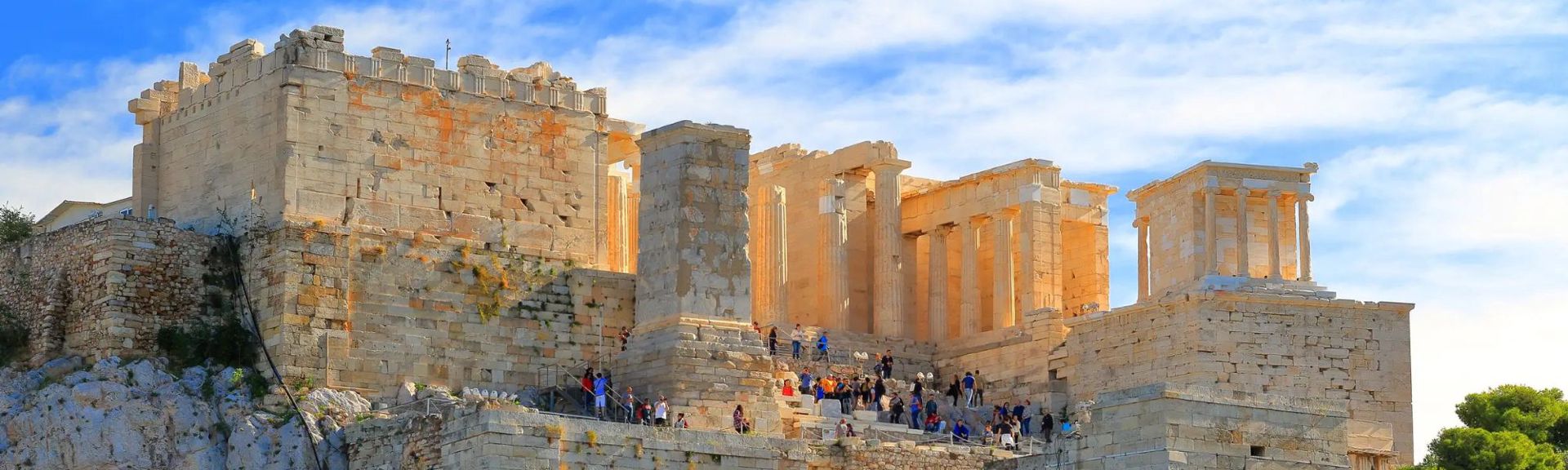 An image of the parthenon on a sunny day filled with people and families who are there to admire the impressive monument in Athens, Greece.