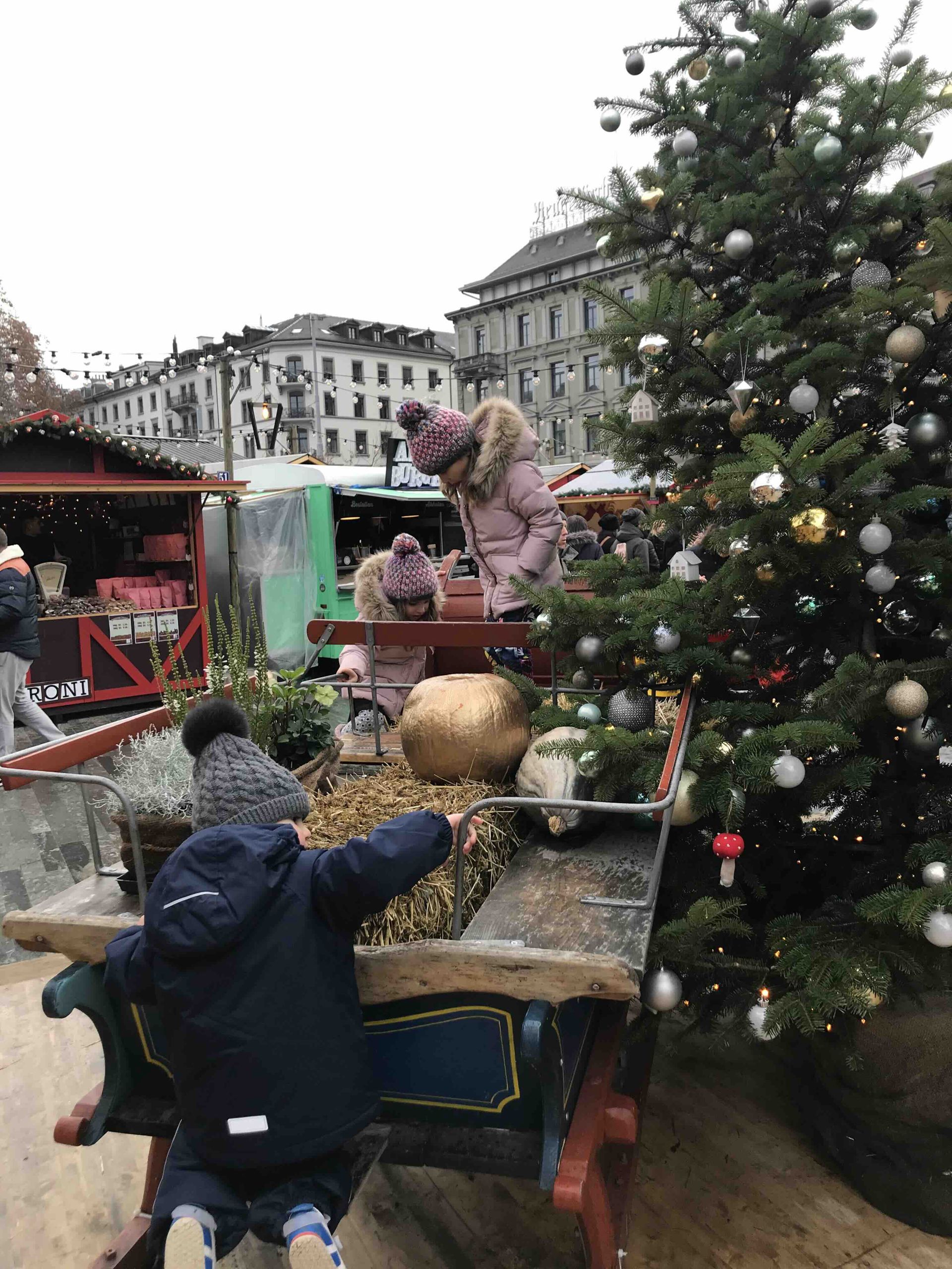 Three kids playing on a Christmas Sledge at Bellevue Christmas Market and Ice Skating Rink in Zurich