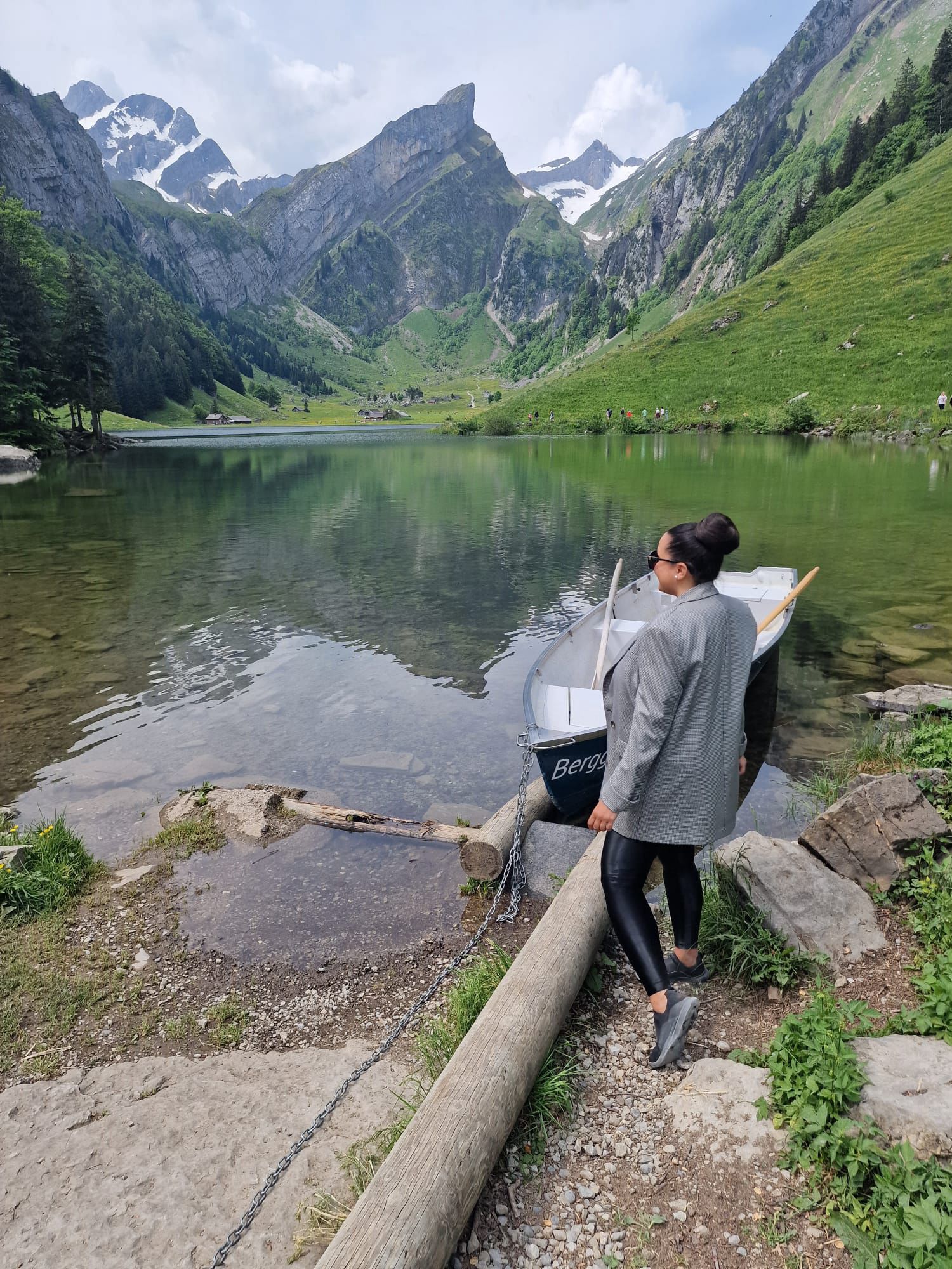 German language teacher standing by a mountain lake in Switzerland, reflecting a calm, nature-inspired approach to learning.