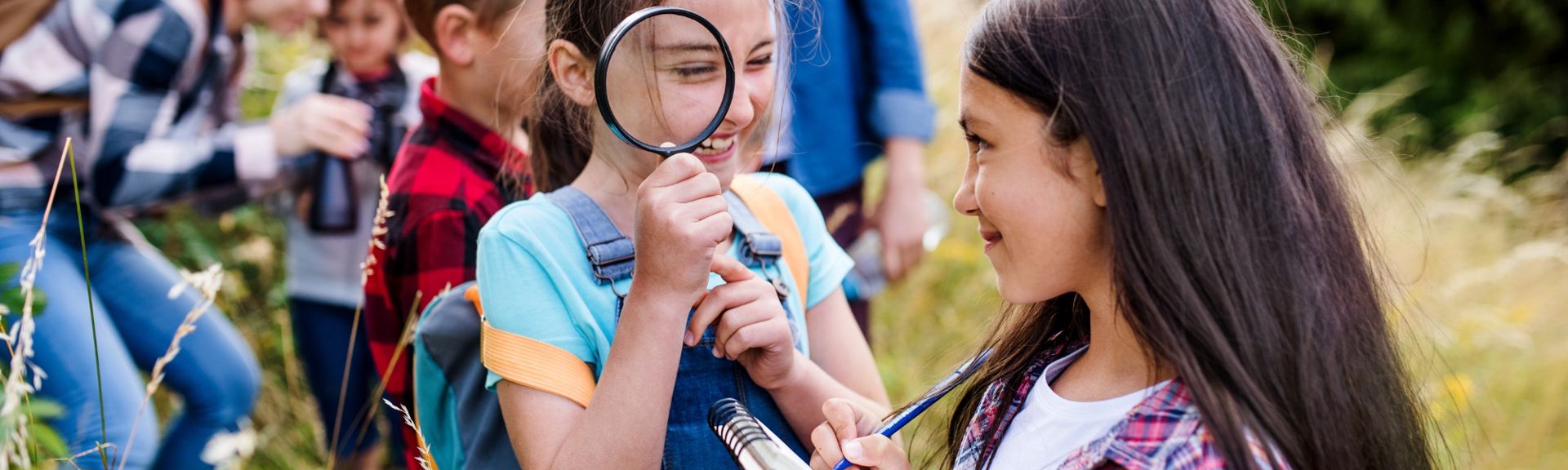 Two girls laughing and exploring outdoors with a magnifying glass during a school activity — a reminder of the curiosity teachers nurture all year long, and why end-of-year teacher gifts matter.