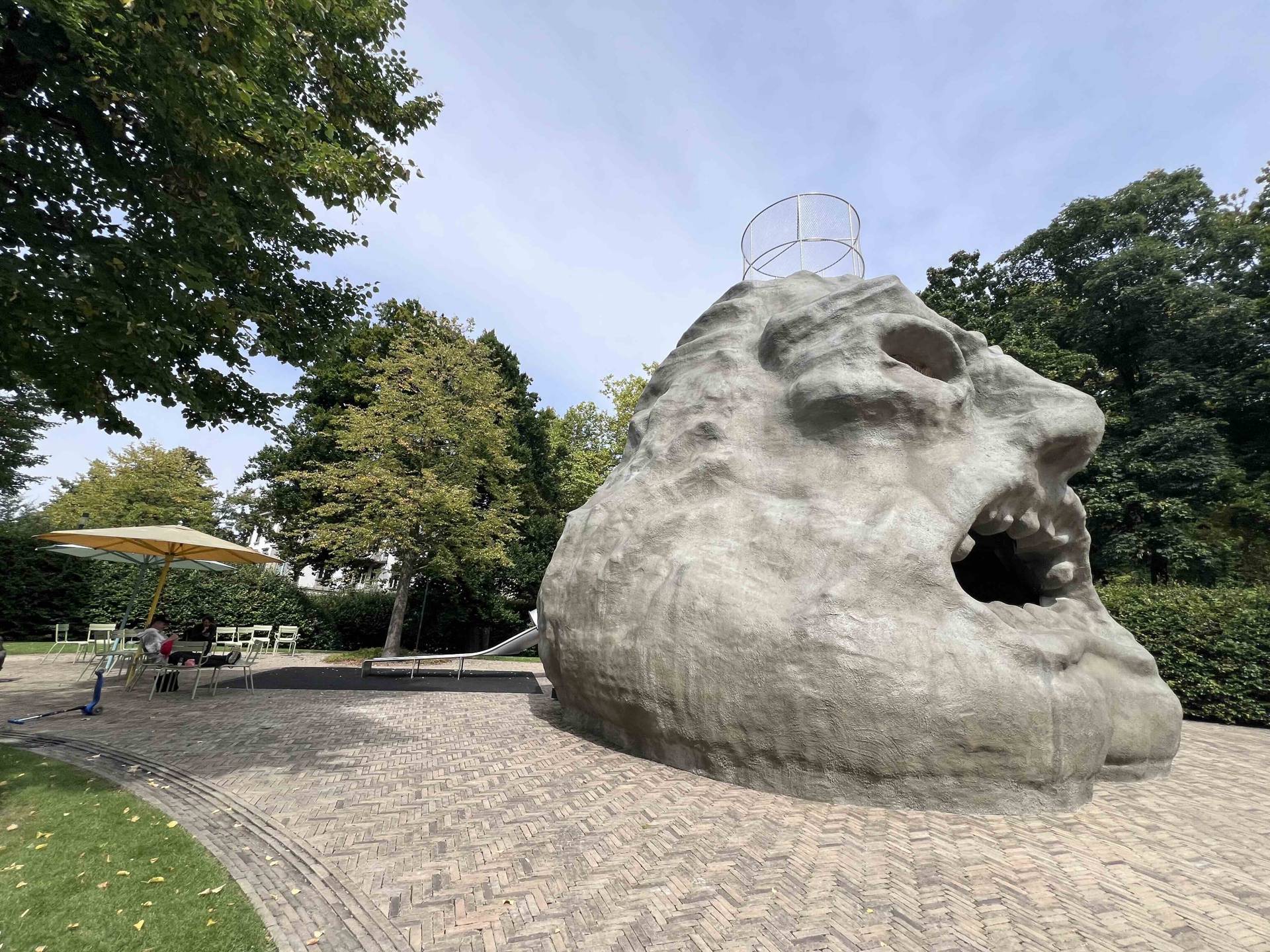 The giant face sculpture holding up the slide sculpture is named Zardos and was designed by the German artist Carsten Höller, at the extension of the Kunsthaus in Zurich, Switzerland.
