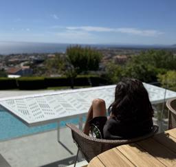 A young boy with long hair looking over a pool into the sea in the distance in Rafina, Greece