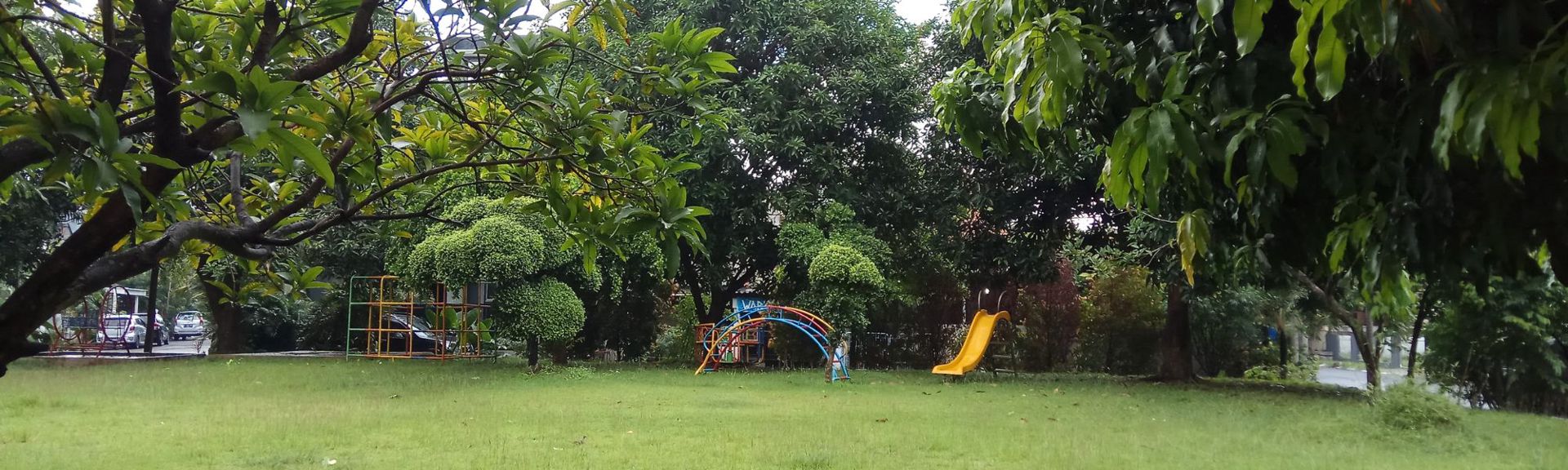 Outdoor children’s playground in the National Garden of Athens, featuring wooden play structures, swings, and slides surrounded by tall trees and lush greenery.