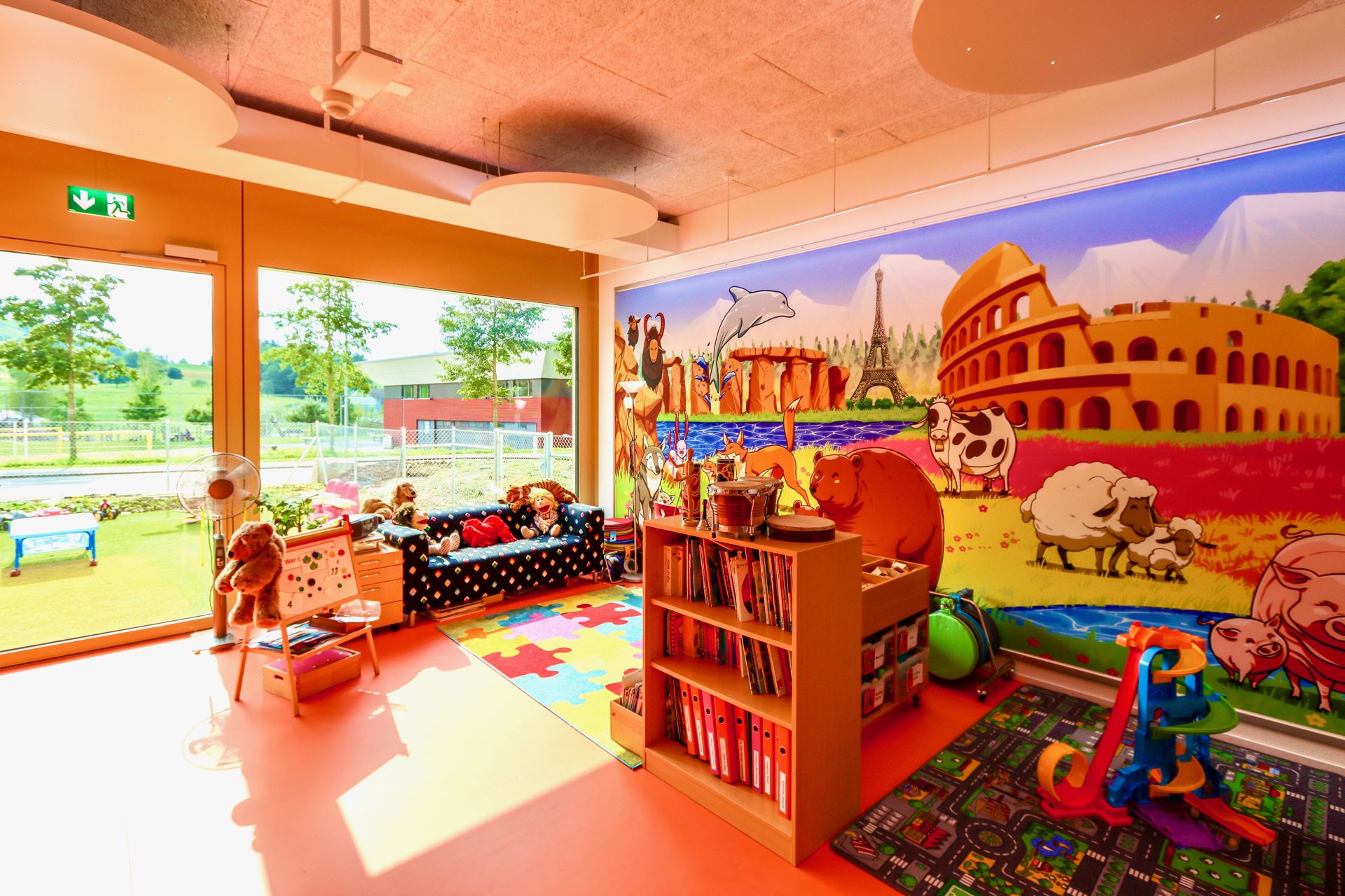 Bright, colourful Kindergarten playroom at OBS in Wollerau with a European landmarks mural, reading corner and play area