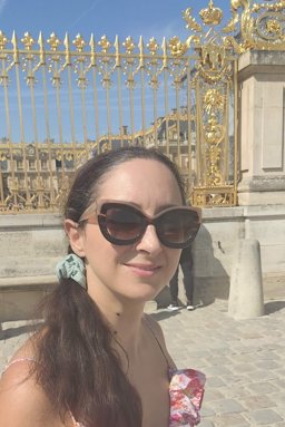 The profile photo of Roubini Charitou with sunglasses on a sunny day in a European city.