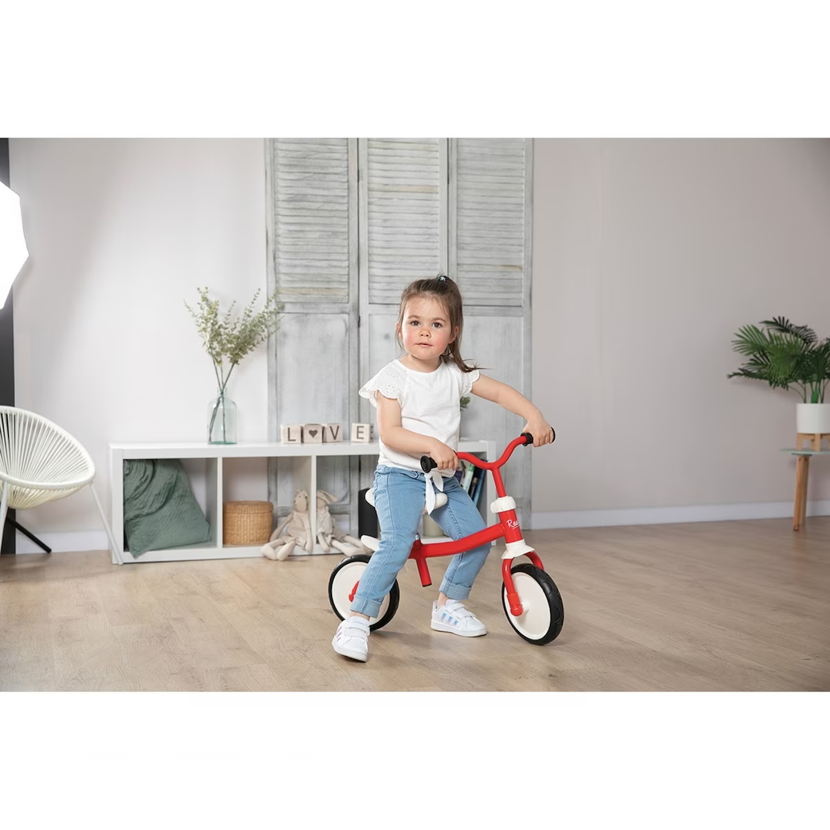 Smoby Rookie Laufrad – robustes Einsteiger-Laufrad in Rot/Weiss, rutschfeste Reifen; Kind fährt drinnen auf Holzfussboden.