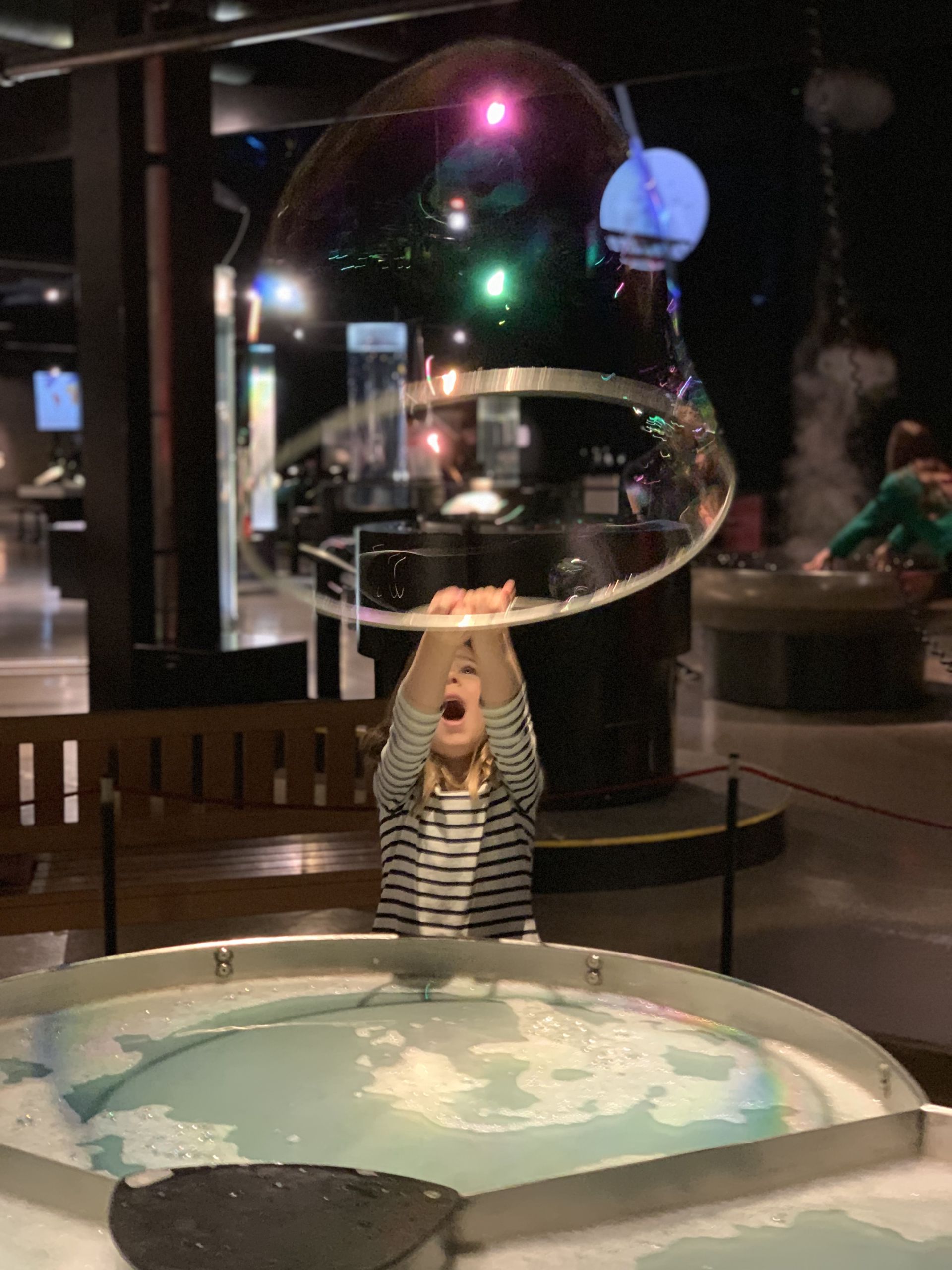 A young girl of about 5 years old is exploring the hydrogen and soap bonds with a giant bubble-making apparatus at the Swiss Science Center Technorama in Winterthur.