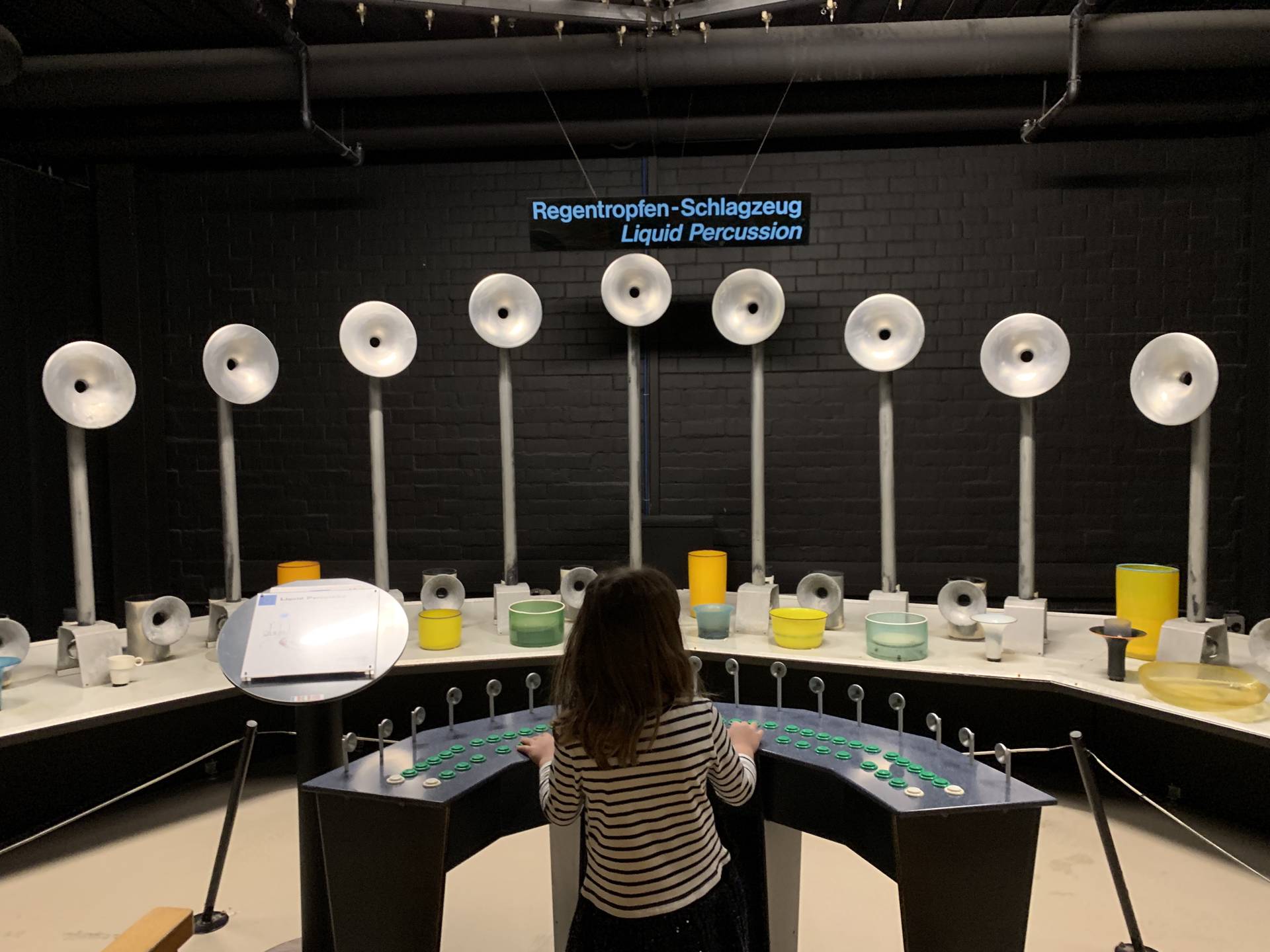 A young girl about 5-6 years old is attempting to play the giant Liquid Percussion instrument at the Swiss Science Center Technorama Museum in Winterthur.  