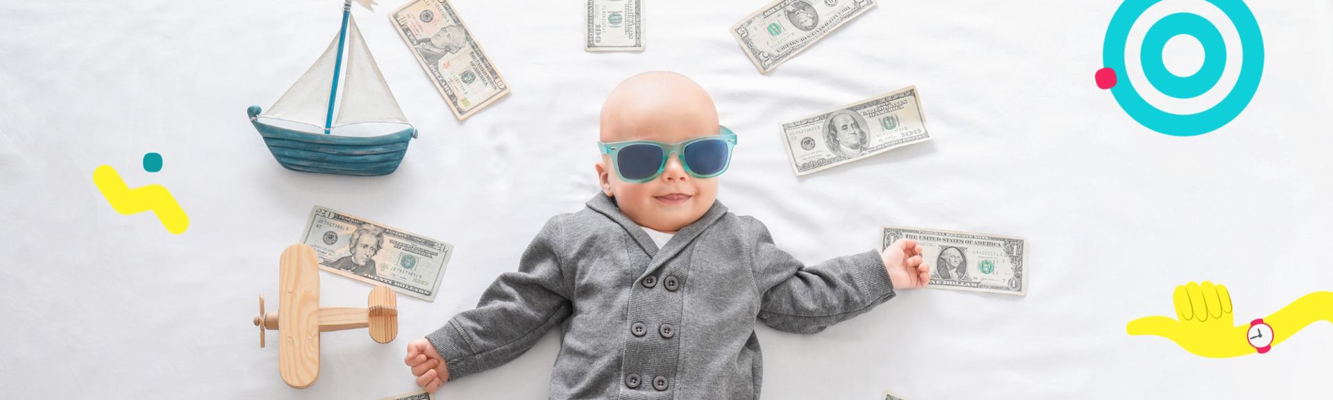Baby wearing sunglasses lying on a bed surrounded by scattered dollar bills, a toy sailboat and a wooden toy plane.