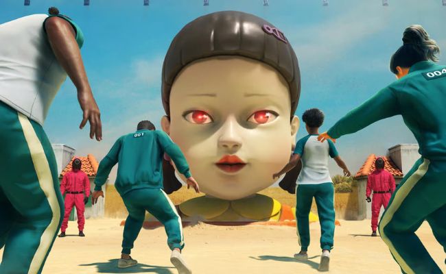 Scene inspired by the Squid Game series showing players in green tracksuits facing a giant doll during the ‘Red Light, Green Light’ game.