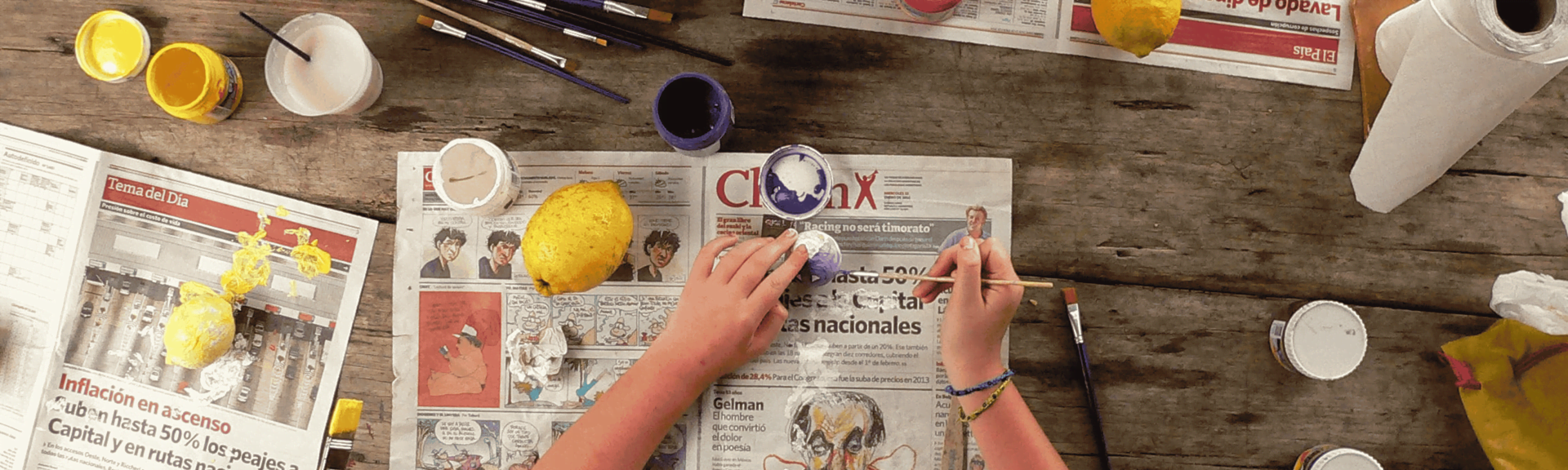 two hands paining a lemon with acrylic paint on a newspaper