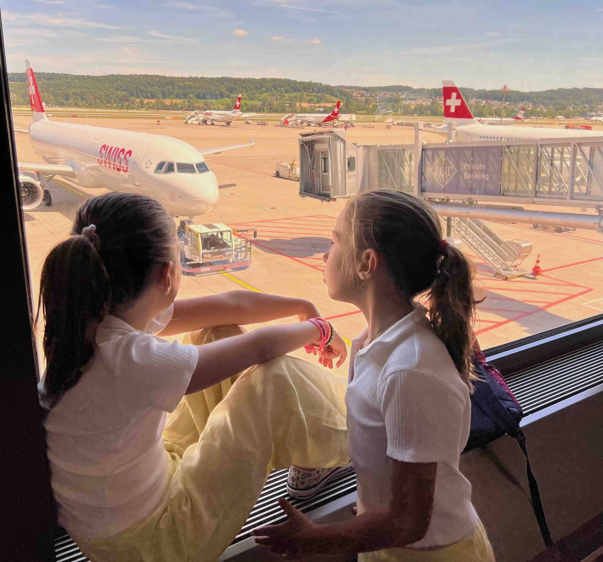 Two girls looking outside the window waiting for their flight at the Family Services Room at Zurich airport