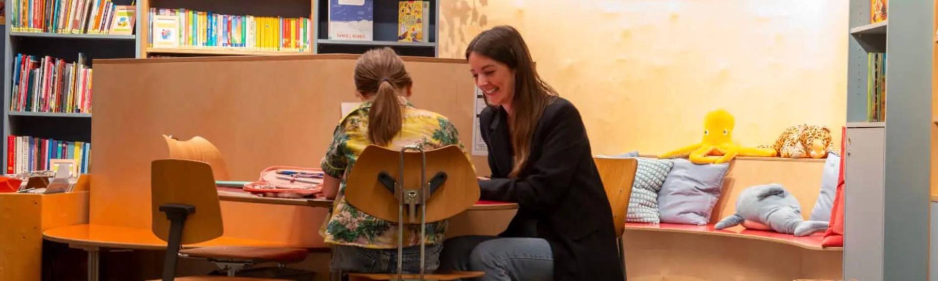 A teacher supports a young student in the reading corner at FOUR Forest Luzern, reflecting the school's individual language support.