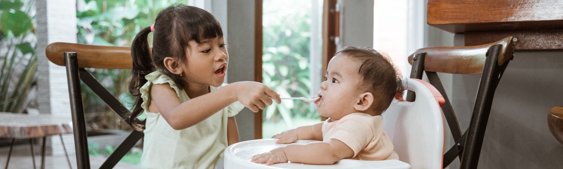 Older sibling helping feed a baby during mealtime, showing care and family bonding.