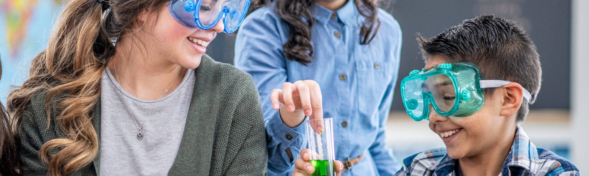 Bilingual primary school students doing a hands-on science experiment with safety goggles