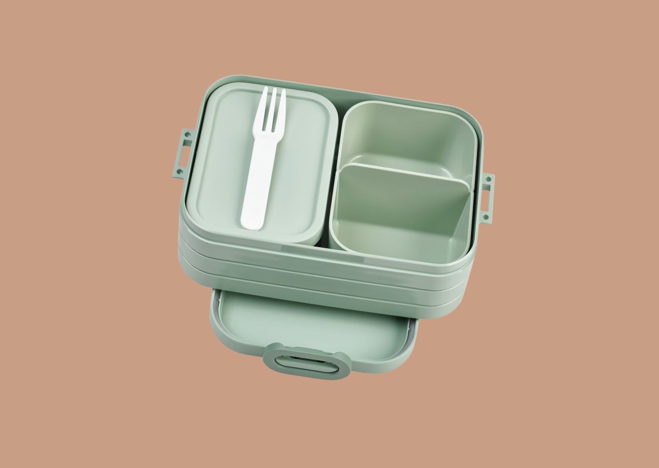 A light green, multi-tiered bento box with a pull-out drawer and separate compartments, displayed on a beige background. A white plastic fork rests on one of the top compartment lids, and the tiers are partially open to showcase the design.