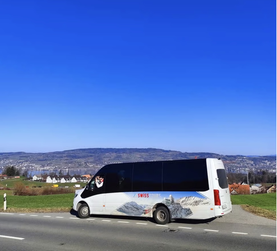 Swiss Tours minibus driving along Lake Zug with mountain views, transport for a Rhine Falls family day trip