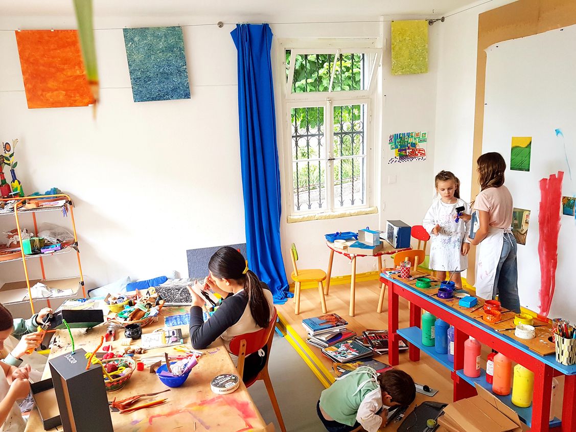 A workshop on a sunny day at Alier Yoku in Vitznau.  It is a colorful space with blue curtains and blank sheets on the wall where children can paint and color freely.  