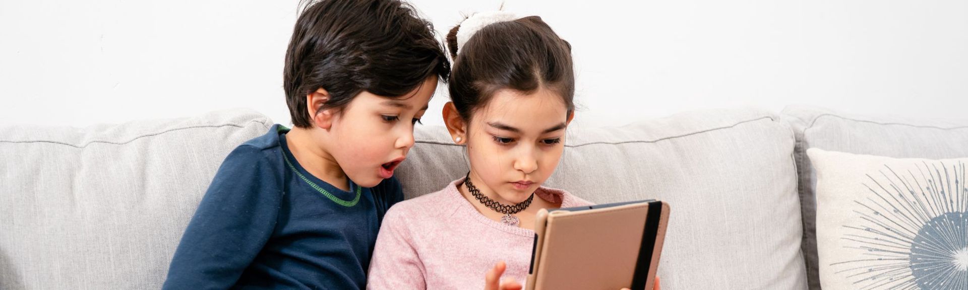Two children sitting on a sofa using a tablet together, illustrating shared screen time and mindful technology use at home.