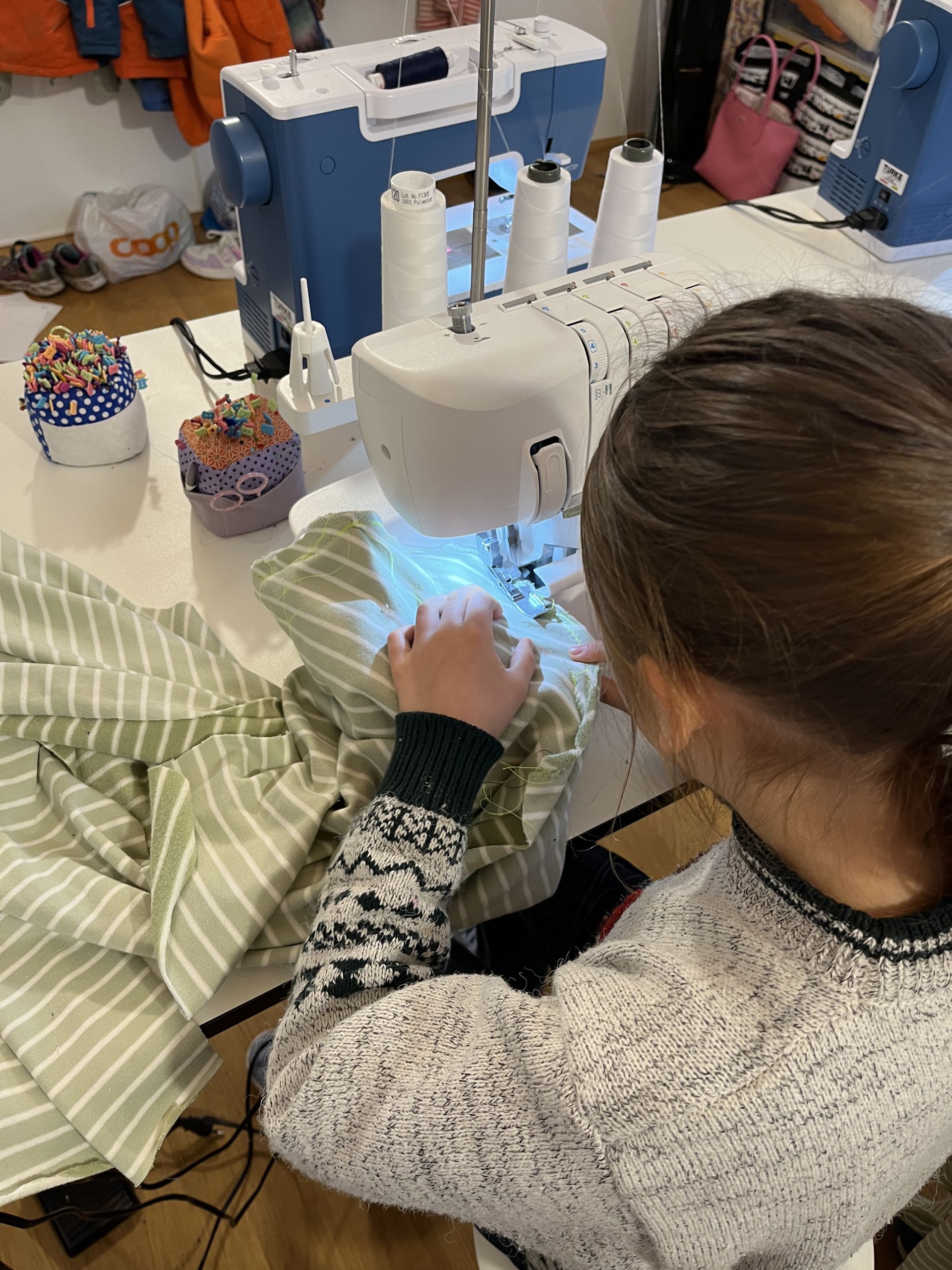 A young girl concentrating as she sews green striped fabric on a sewing machine during a knit.sew class in Zurich.