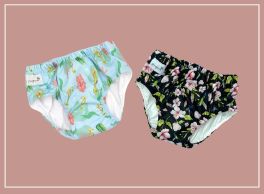 Two baby swim diapers displayed side-by-side on a light reddish-brown background with a white border. The left diaper is light blue with green and orange sea-themed patterns, while the right diaper is black with pink and white floral patterns. Both have white elasticized leg openings and waistbands, showcasing their soft, fabric-like texture.