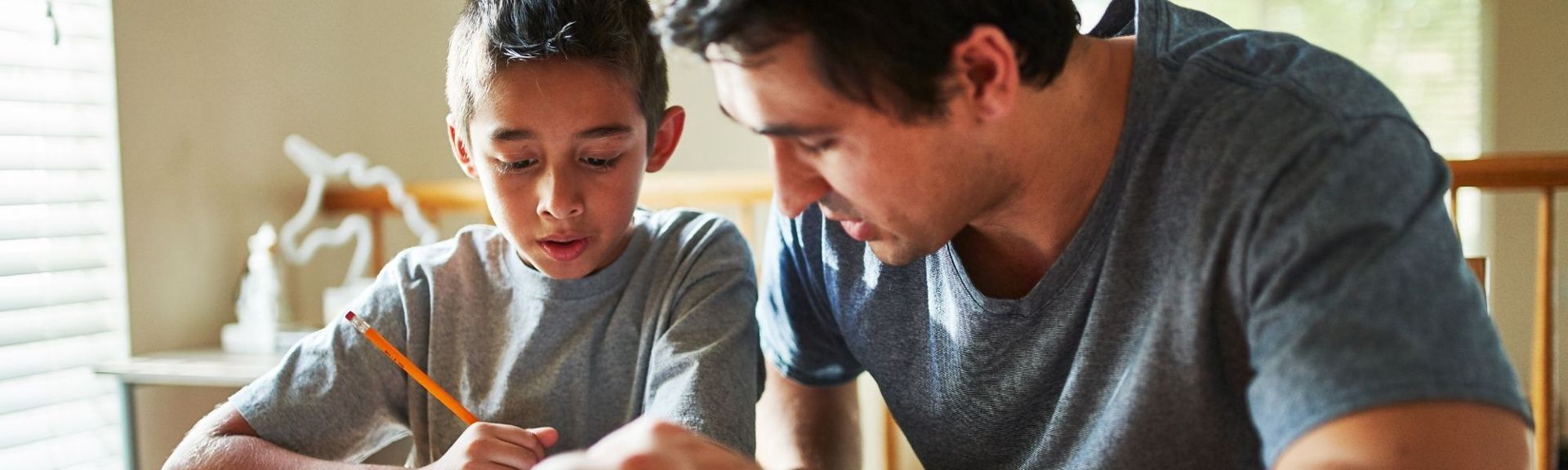 Parent sitting with a child at a table, helping with homework and learning activities at home.