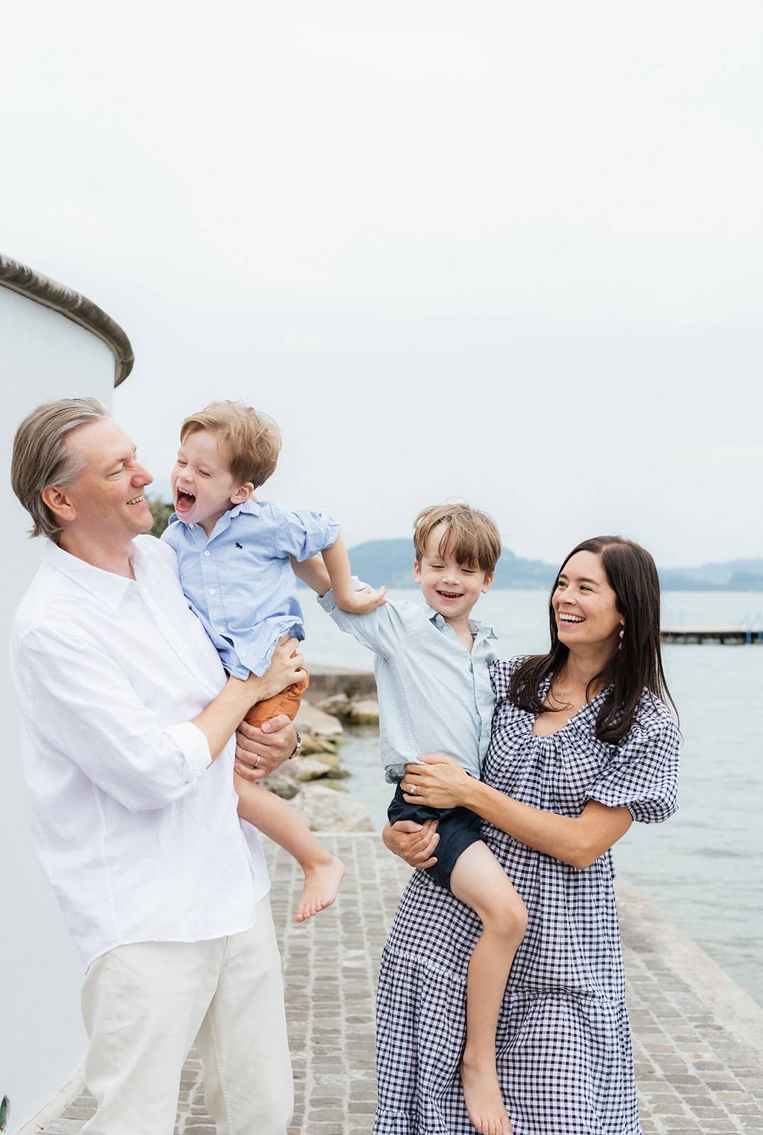 A family photo with a dad, mom and two boys in their arms in the old town of Zurich. It is a spontaneous one evoking memories and fun times are the boys look active and very playful.  It is captured by family photographer in Switzerland, Mary Fernandez.