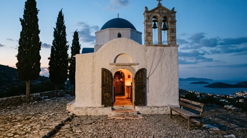 A whitewashed chapel with a blue dome and bell tower at dusk, its door open to a candlelit interior above an island bay