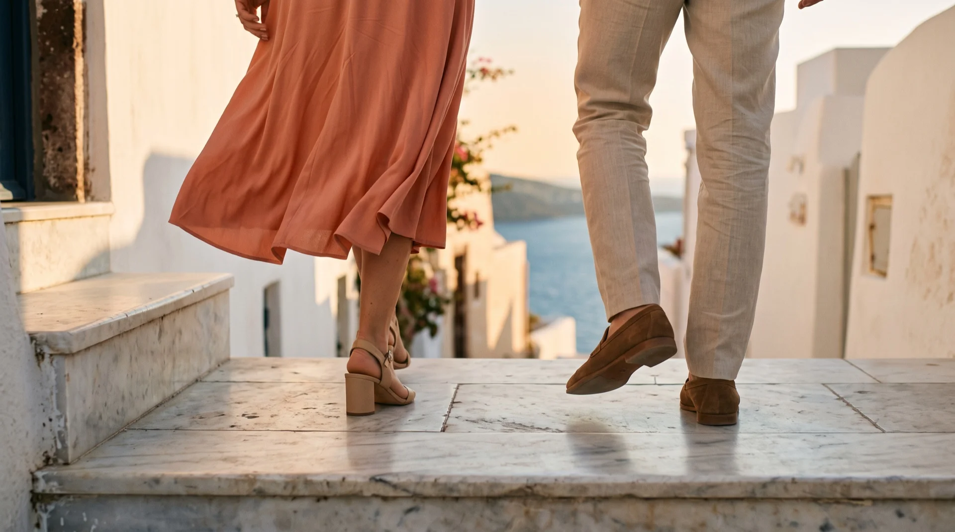 Καλεσμένοι σε μαρμάρινα σκαλιά νησιού: κοραλί φόρεμα με σανδάλια με χοντρό τακούνι και λινό παντελόνι με σουέτ μοκασίνια