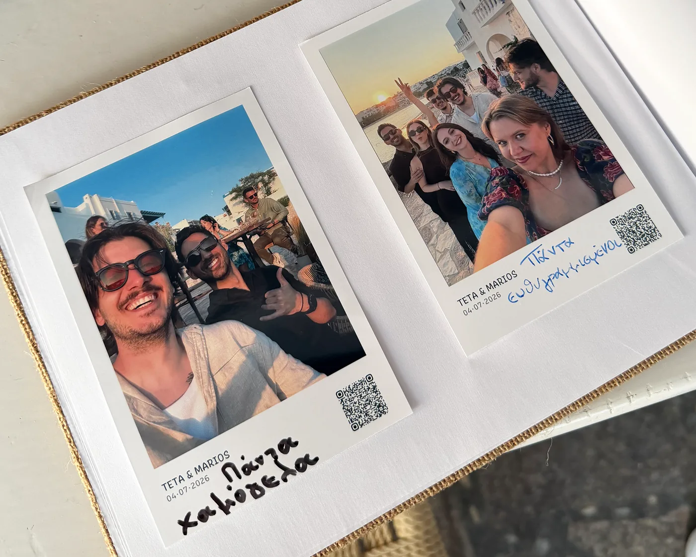An open wedding guest book with two Smart Print photo cards glued onto the page, each captioned Teta and Marios with a QR code, and handwritten Greek wishes beside them