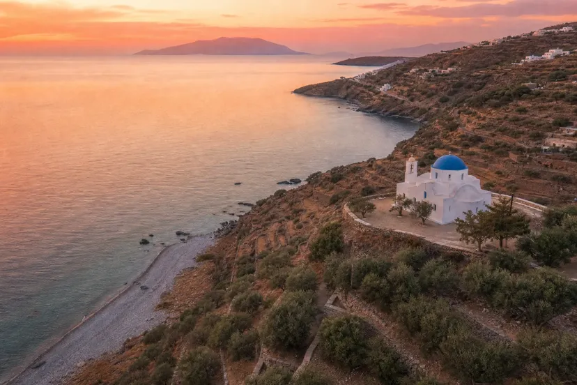 Sun-drenched Greek coastline at golden hour with a hilltop wedding venue overlooking the Aegean Sea