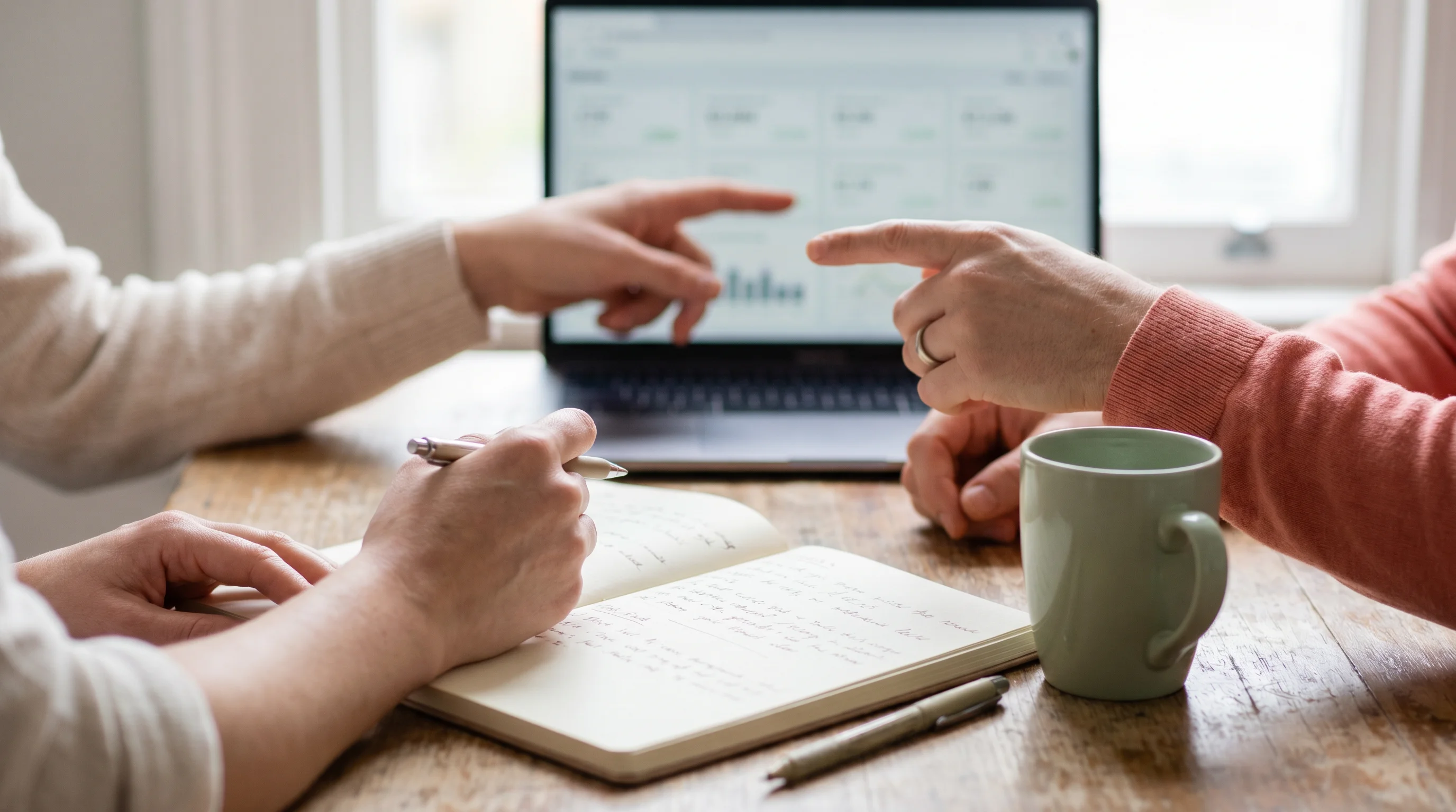 Hands reviewing a wedding budget on a laptop next to coffee and a notebook